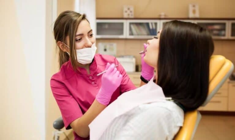 Dental hygienist in pink gloves and mask examines patient's teeth in modern dental office.