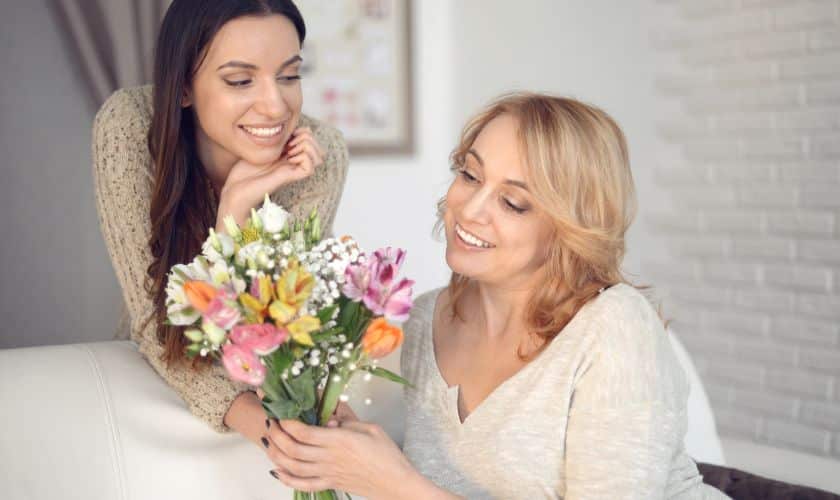 Two women smiling while holding colorful flowers in a bright dental office setting.