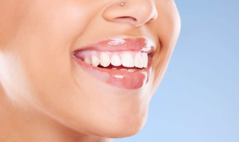 Close-up of person smiling brightly, displaying healthy white teeth against blue background.